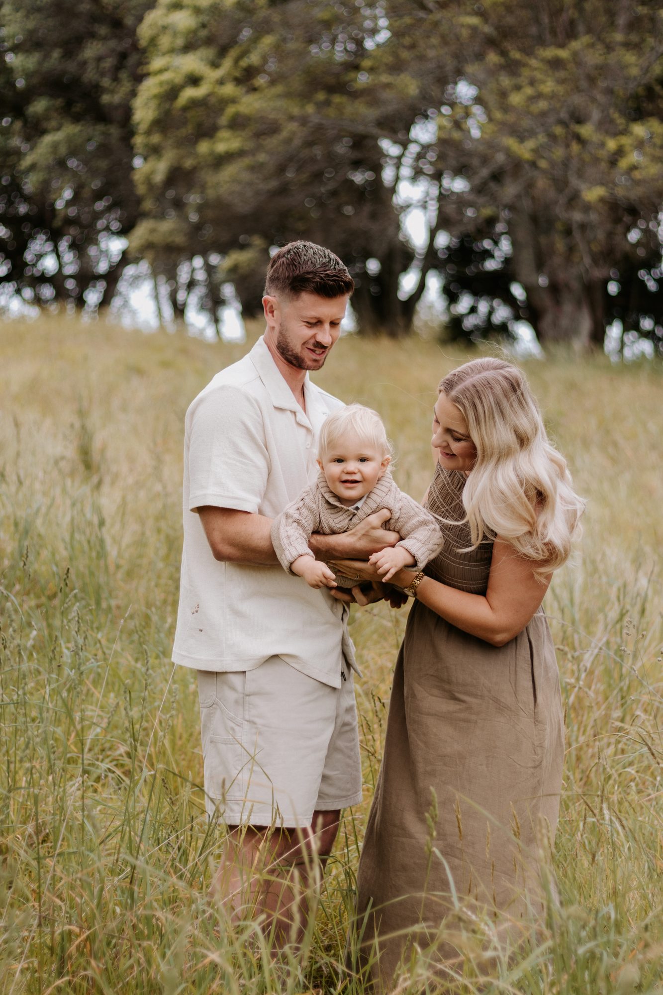 Parents smiling at their toddler son while standing together in a grassy field